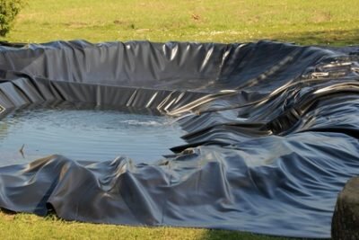 Gartenteichfolie, die in einen Gartenteich gelegt wirde. Wasser im Teich drückt die Folie in alle Kanten. Die Folie steht noch über und muss auf die passende größe Zugeschnitten werden.