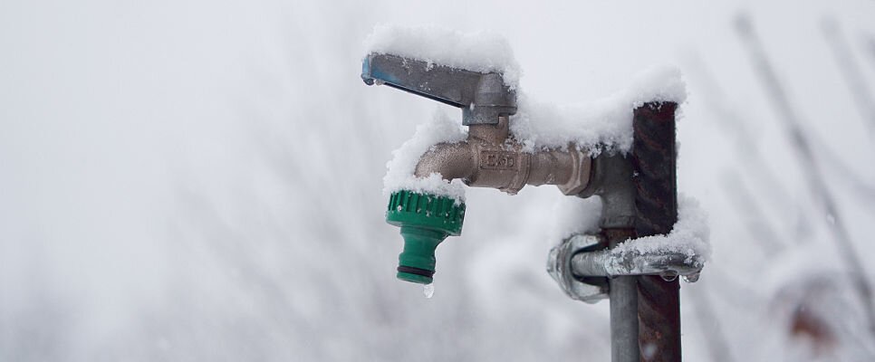 Ein mit schnee bedeckter Gartenwasserhahn mit einer...